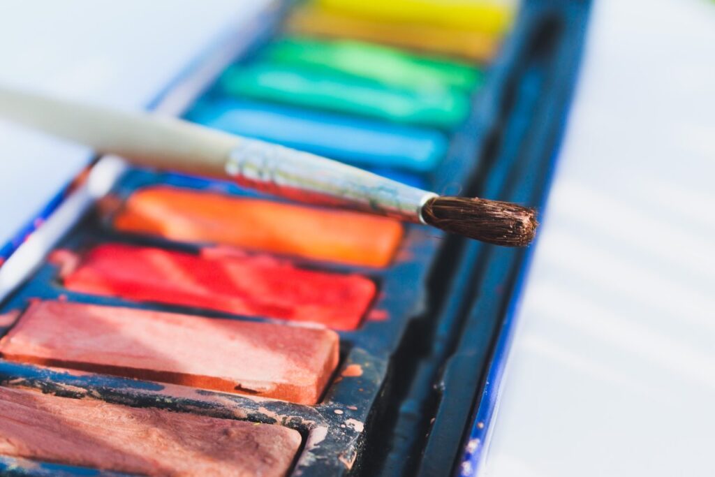 the photo shows a paintbrush resting on a selection of paint colours