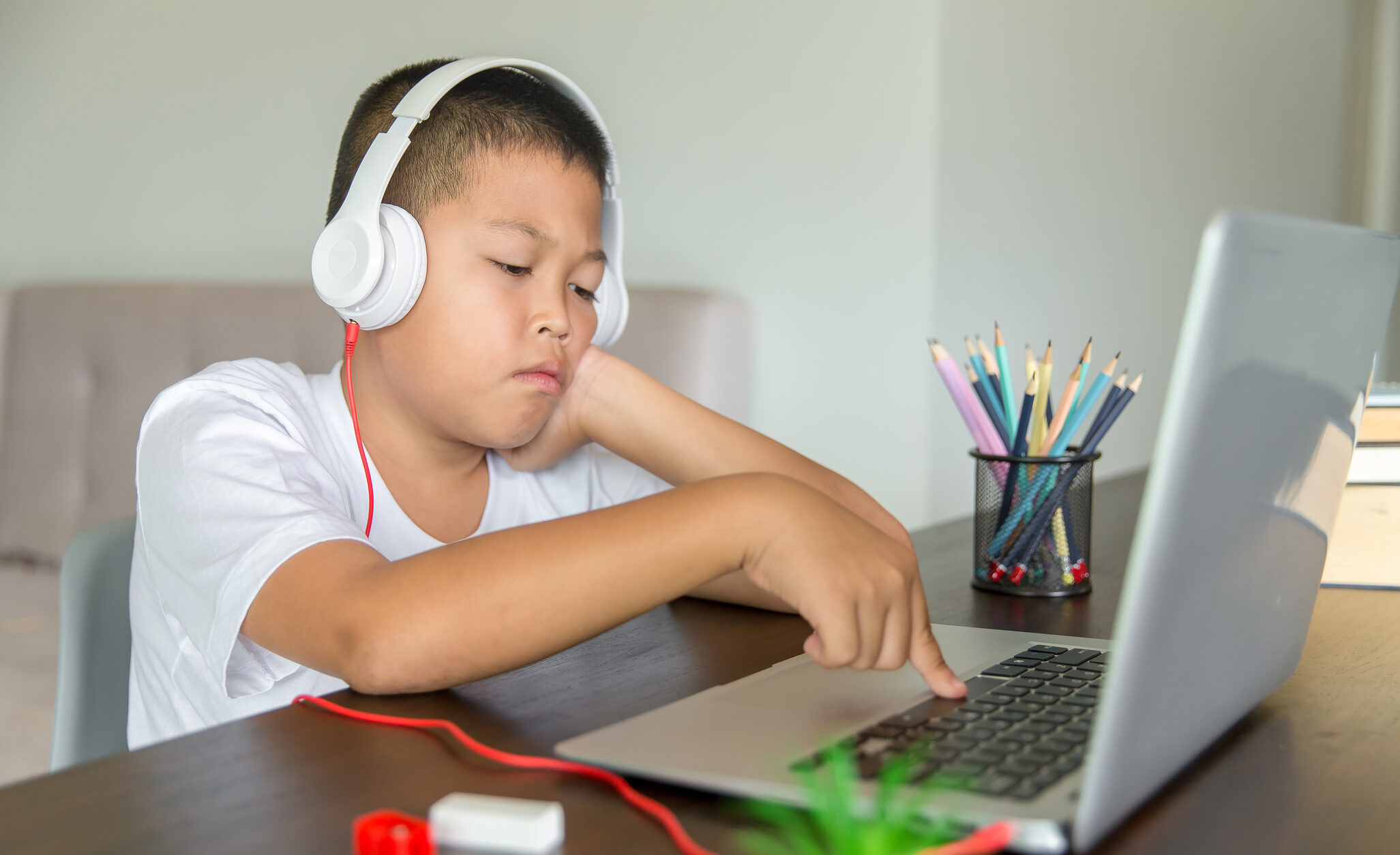 the photo shows a boy with short dark hair who is wearing white headphones and pressing the space bar on a laptop computer